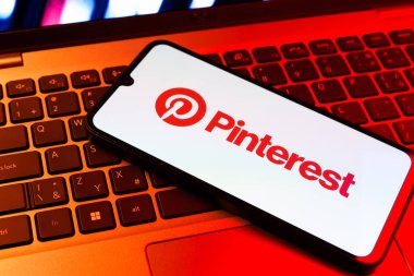 Prag, Çek Cumhuriyeti - 09 02 2025: Pinterest logosunun renkli ışıklarla aydınlatıldığı dizüstü bilgisayardaki telefon. Pinterest fikirleri görsel olarak keşfetmek ve kaydetmek için bir platformdur..