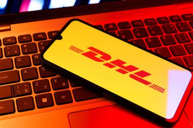 Prag, Çek Cumhuriyeti - 09 02 2025: DHL logosu renkli ışık tarafından yakılan dizüstü bilgisayardaki telefon. DHL uluslararası nakliye hizmeti sunan bir lojistik şirketidir..