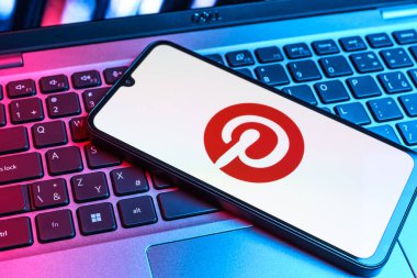 Prag, Çek Cumhuriyeti - 09 02 2025: Pinterest logosunun renkli ışıklarla aydınlatıldığı dizüstü bilgisayardaki telefon. Pinterest fikirleri görsel olarak keşfetmek ve kaydetmek için bir platformdur..