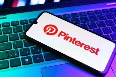 Prag, Çek Cumhuriyeti - 09 02 2025: Pinterest logosunun renkli ışıklarla aydınlatıldığı dizüstü bilgisayardaki telefon. Pinterest fikirleri görsel olarak keşfetmek ve kaydetmek için bir platformdur..