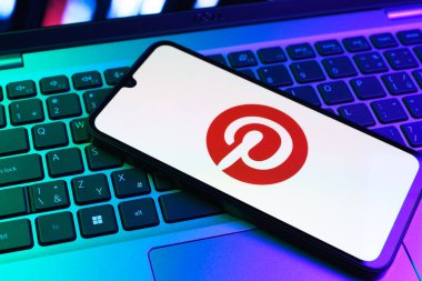 Prag, Çek Cumhuriyeti - 09 02 2025: Pinterest logosunun renkli ışıklarla aydınlatıldığı dizüstü bilgisayardaki telefon. Pinterest fikirleri görsel olarak keşfetmek ve kaydetmek için bir platformdur..