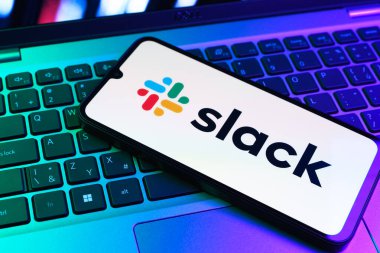 Prag, Çek Cumhuriyeti - 09 02 2025: Renkli ışık tarafından yakılan dizüstü bilgisayardaki telefon Slack logosunu gösteriyor. Slack takım mesajlaşması ve iş yeri iletişimi için bir platformdur.