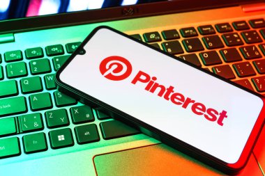 Prag, Çek Cumhuriyeti - 09 02 2025: Pinterest logosunun renkli ışıklarla aydınlatıldığı dizüstü bilgisayardaki telefon. Pinterest fikirleri görsel olarak keşfetmek ve kaydetmek için bir platformdur..