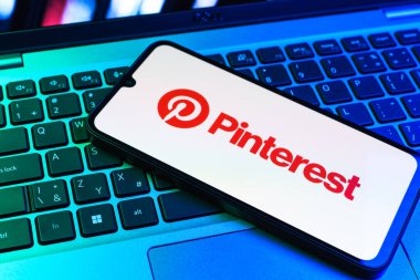 Prag, Çek Cumhuriyeti - 09 02 2025: Pinterest logosunun renkli ışıklarla aydınlatıldığı dizüstü bilgisayardaki telefon. Pinterest fikirleri görsel olarak keşfetmek ve kaydetmek için bir platformdur..