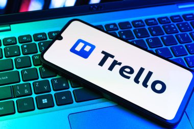 Prag, Çek Cumhuriyeti - 09 02 2025: Renkli ışık tarafından yakılan dizüstü bilgisayardaki telefon Trello logosunu gösteriyor. Trello, tahta ve görevleri kullanarak proje yönetimi için bir platformdur.