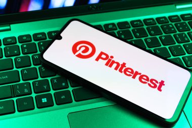 Prag, Çek Cumhuriyeti - 09 02 2025: Pinterest logosunun renkli ışıklarla aydınlatıldığı dizüstü bilgisayardaki telefon. Pinterest fikirleri görsel olarak keşfetmek ve kaydetmek için bir platformdur..