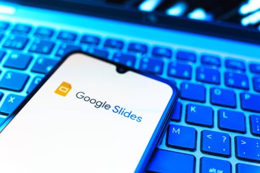 Prag, Çek Cumhuriyeti - 08 19 2025: Google Slides logosunu gösteren klavyenin üzerinde duran cep telefonunun yakından görüntüsü. Google Slides sunumlar ve slayt gösterileri oluşturmak için bir platformdur.