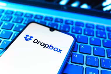 Prag, Çek Cumhuriyeti - 08 19 2025: Dropbox logosunu gösteren klavyenin üzerinde duran cep telefonunun yakından görüntüsü. Dropbox bulut depolama ve dosya paylaşımı için bir platformdur.
