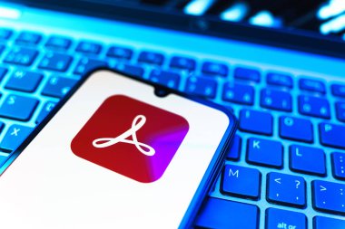 Prag, Çek Cumhuriyeti - 08 19 2025: Klavyede duran ve Akrobat Reader logosunu gösteren cep telefonunun yakından görüntüsü. Acrobat Reader, PDF belgelerini görüntülemek ve yönetmek için bir platformdur.