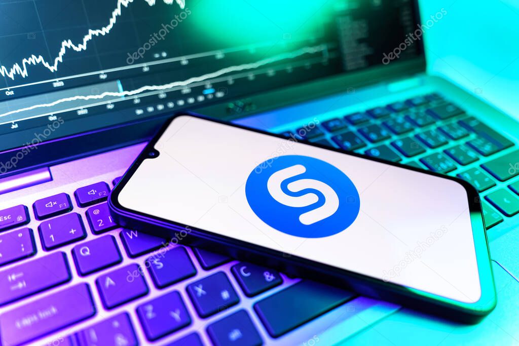 Prague, Czechia - 09 02 2025: Phone on laptop with stock chart showing Shazam logo. Shazam is an app for identifying songs and music tracks.