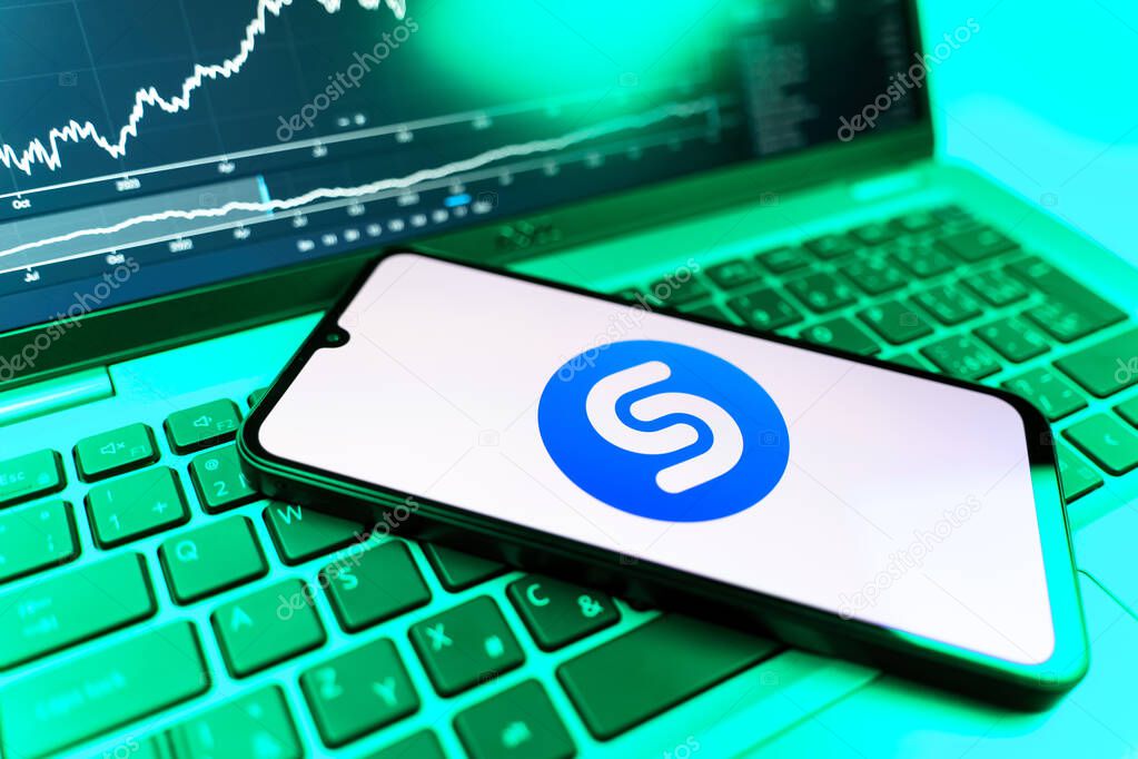 Prague, Czechia - 09 02 2025: Phone on laptop with stock chart showing Shazam logo. Shazam is an app for identifying songs and music tracks.