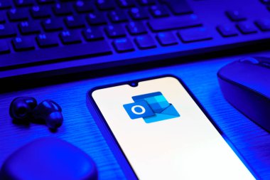 Prague, Czechia - 08 12 2025: A side view of a desk with a keyboard and a mobile phone displaying the Outlook logo. Outlook is an email platform for sending and managing messages.