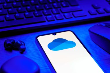 Prague, Czechia - 08 12 2025: A side view of a desk with a keyboard and a mobile phone displaying the OneDrive logo. OneDrive is a cloud storage platform for saving and sharing files.