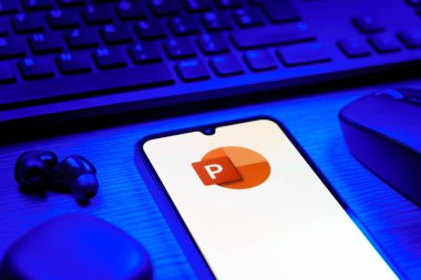 Prague, Czechia - 08 12 2025: A side view of a desk with a keyboard and a mobile phone displaying the Powerpoint logo. Powerpoint is a software for creating presentations and slideshows.