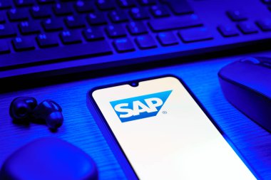 Prag, Çek Cumhuriyeti - 08 12 2025: SAP logosunu gösteren klavyesi ve cep telefonu olan bir masanın yan görüntüsü. SAP, şirket uygulamaları ve çözümleri sağlayan bir yazılım şirketidir..