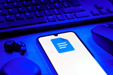 Prag, Çek Cumhuriyeti - 08 12 2025: Google Docs logosunu gösteren klavyesi ve cep telefonu olan bir masanın yan görüntüsü. Google Docs metin belgeleri oluşturmak ve düzenlemek için bir platformdur.