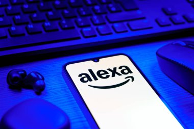 Prag, Çek Cumhuriyeti - 08 12 2025: Alexa logosunu gösteren klavyesi ve cep telefonu olan bir masanın yan görüntüsü. Alexa akıllı aygıtlar ve servisler için ses asistanıdır.