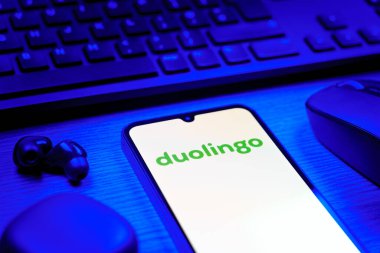 Prag, Çek Cumhuriyeti - 08 12 2025: Duolingo logosunu gösteren klavyesi ve cep telefonu olan bir masanın yan görüntüsü. Duolingo interaktif olarak dil öğrenmek için bir platformdur..