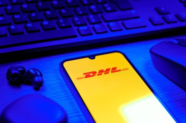 Prag, Çek Cumhuriyeti - 08 12 2025: DHL logosunu gösteren klavyesi ve cep telefonu olan bir masanın yan görüntüsü. DHL uluslararası nakliye hizmeti sunan bir lojistik şirketidir..