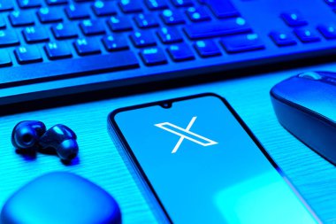 Prague, Czechia - 08 12 2025: A side view of a desk with a keyboard and a mobile phone displaying the X logo. X is a platform for sharing short posts and updates.