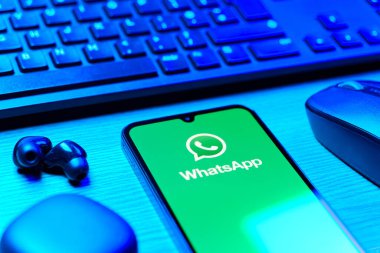 Prague, Czechia - 08 12 2025: A side view of a desk with a keyboard and a mobile phone displaying the WhatsApp logo. WhatsApp is an app for sending texts, calls, and media.