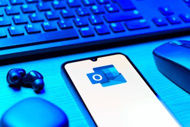 Prague, Czechia - 08 12 2025: A side view of a desk with a keyboard and a mobile phone displaying the Outlook logo. Outlook is an email platform for sending and managing messages.
