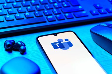 Prague, Czechia - 08 12 2025: A side view of a desk with a keyboard and a mobile phone displaying the Teams logo. Teams is a platform for team collaboration, meetings, and communication.