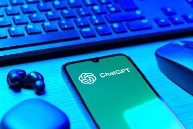 Prague, Czechia - 08 12 2025: A side view of a desk with a keyboard and a mobile phone displaying the ChatGPT logo. ChatGPT is an AI chatbot for generating text and answering questions.