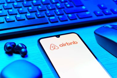 Prag, Çek Cumhuriyeti - 08 12 2025: Airbnb logosunu gösteren klavyesi ve cep telefonu olan bir masanın yan görüntüsü. Airbnb dünya çapında kısa vadeli konaklama için bir platformdur..