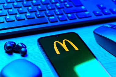 Prag, Çek Cumhuriyeti - 08 12 2025: McDonalds logosunu gösteren klavyesi ve cep telefonu olan bir masanın yan görüntüsü. McDonalds hamburger, patates kızartması ve daha fazlası sunan bir fast-food zinciri..
