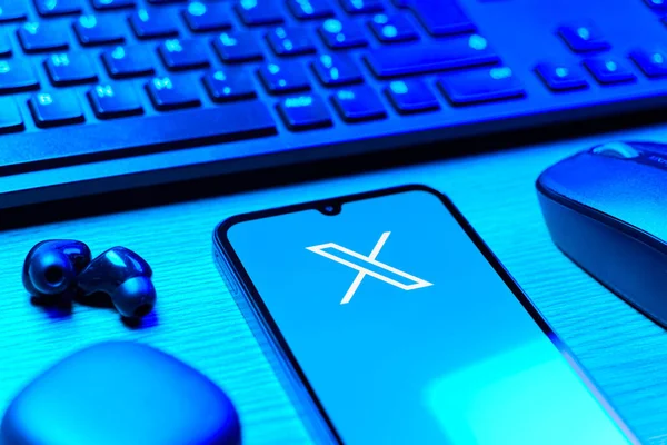 Prague, Czechia - 08 12 2025: A side view of a desk with a keyboard and a mobile phone displaying the X logo. X is a platform for sharing short posts and updates.