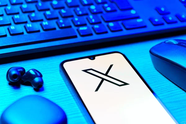 Prague, Czechia - 08 12 2025: A side view of a desk with a keyboard and a mobile phone displaying the X logo. X is a platform for sharing short posts and updates.