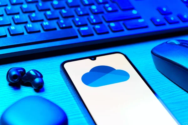 Prague, Czechia - 08 12 2025: A side view of a desk with a keyboard and a mobile phone displaying the OneDrive logo. OneDrive is a cloud storage platform for saving and sharing files.