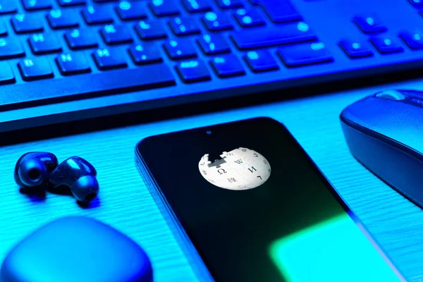 Prag, Çek Cumhuriyeti - 08 12 2025: Vikipedi logosunu gösteren klavyesi ve cep telefonu olan bir masanın yan görüntüsü. Vikipedi çevrimiçi bir ansiklopedidir..