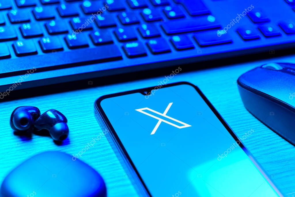 Prague, Czechia - 08 12 2025: A side view of a desk with a keyboard and a mobile phone displaying the X logo. X is a platform for sharing short posts and updates.