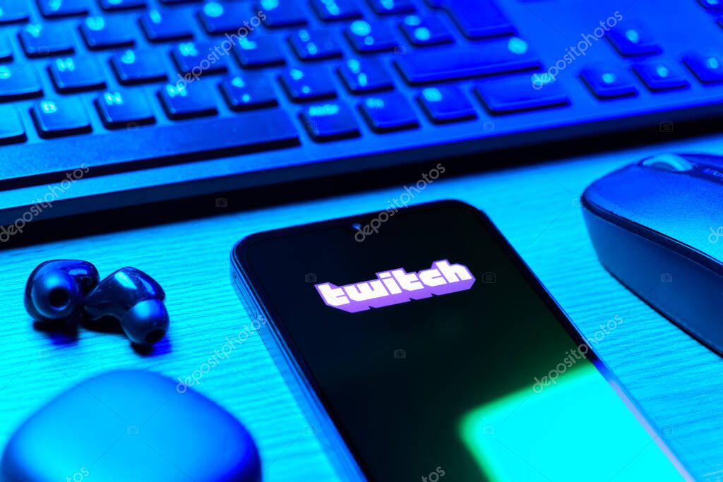 Prague, Czechia - 08 12 2025: A side view of a desk with a keyboard and a mobile phone displaying the Twitch logo. Twitch is a platform for live streaming games and content.