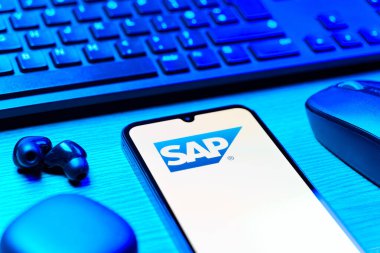 Prag, Çek Cumhuriyeti - 08 12 2025: SAP logosunu gösteren klavyesi ve cep telefonu olan bir masanın yan görüntüsü. SAP, şirket uygulamaları ve çözümleri sağlayan bir yazılım şirketidir..
