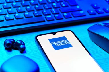 Prag, Çek Cumhuriyeti - 08 12 2025: Amerikan Ekspres logosunu gösteren klavyesi ve cep telefonu olan bir masanın yan görüntüsü. American Express kart ve bankacılık sunan bir finans şirketidir..