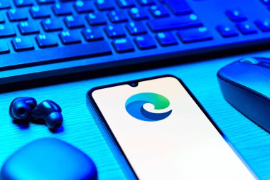 Prag, Çek Cumhuriyeti - 08 12 2025: Kenar logosunu gösteren klavyesi ve cep telefonu olan bir masanın yan görüntüsü. Edge, Microsoft tarafından Windows aygıtları için geliştirilen bir web tarayıcısıdır..