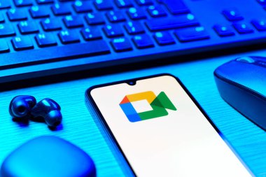 Prag, Çek Cumhuriyeti - 08 12 2025: Google Meet logosunu gösteren klavyesi ve cep telefonu olan bir masanın yan görüntüsü. Google Meet video toplantıları ve çevrimiçi işbirliği için bir platformdur.