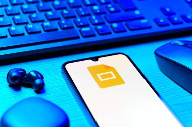 Prag, Çek Cumhuriyeti - 08 12 2025: Google Slides logosunu gösteren klavyesi ve cep telefonu olan bir masanın yan görüntüsü. Google Slides sunumlar ve slayt gösterileri oluşturmak için bir platformdur.
