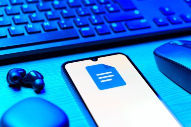 Prag, Çek Cumhuriyeti - 08 12 2025: Google Docs logosunu gösteren klavyesi ve cep telefonu olan bir masanın yan görüntüsü. Google Docs metin belgeleri oluşturmak ve düzenlemek için bir platformdur.