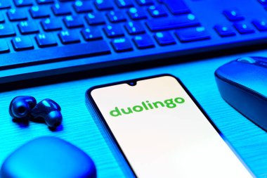 Prag, Çek Cumhuriyeti - 08 12 2025: Duolingo logosunu gösteren klavyesi ve cep telefonu olan bir masanın yan görüntüsü. Duolingo interaktif olarak dil öğrenmek için bir platformdur..