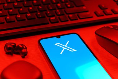 Prague, Czechia - 08 12 2025: A side view of a desk with a keyboard and a mobile phone displaying the X logo. X is a platform for sharing short posts and updates.