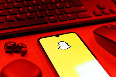 Prague, Czechia - 08 12 2025: A side view of a desk with a keyboard and a mobile phone displaying the Snapchat logo. Snapchat is an app for sending photos, videos, and temporary messages.
