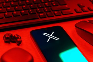 Prague, Czechia - 08 12 2025: A side view of a desk with a keyboard and a mobile phone displaying the X logo. X is a platform for sharing short posts and updates.