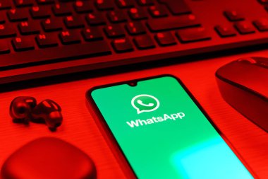Prague, Czechia - 08 12 2025: A side view of a desk with a keyboard and a mobile phone displaying the WhatsApp logo. WhatsApp is an app for sending texts, calls, and media.