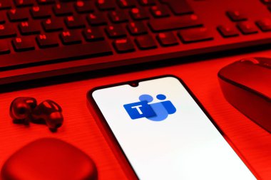 Prague, Czechia - 08 12 2025: A side view of a desk with a keyboard and a mobile phone displaying the Teams logo. Teams is a platform for team collaboration, meetings, and communication.