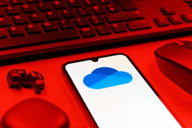 Prague, Czechia - 08 12 2025: A side view of a desk with a keyboard and a mobile phone displaying the OneDrive logo. OneDrive is a cloud storage platform for saving and sharing files.