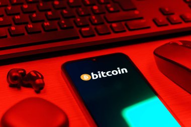 Prag, Çek Cumhuriyeti - 08 12 2025: Bitcoin logosunu gösteren klavyesi ve cep telefonu olan bir masanın yan görüntüsü. Bitcoin merkezi olmayan işlemler için dijital bir kripto para birimidir.